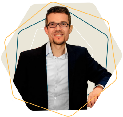 Ein Mann mit Brille in einem schwarzen Anzug, der lächelt und an einem Tisch sitzt.